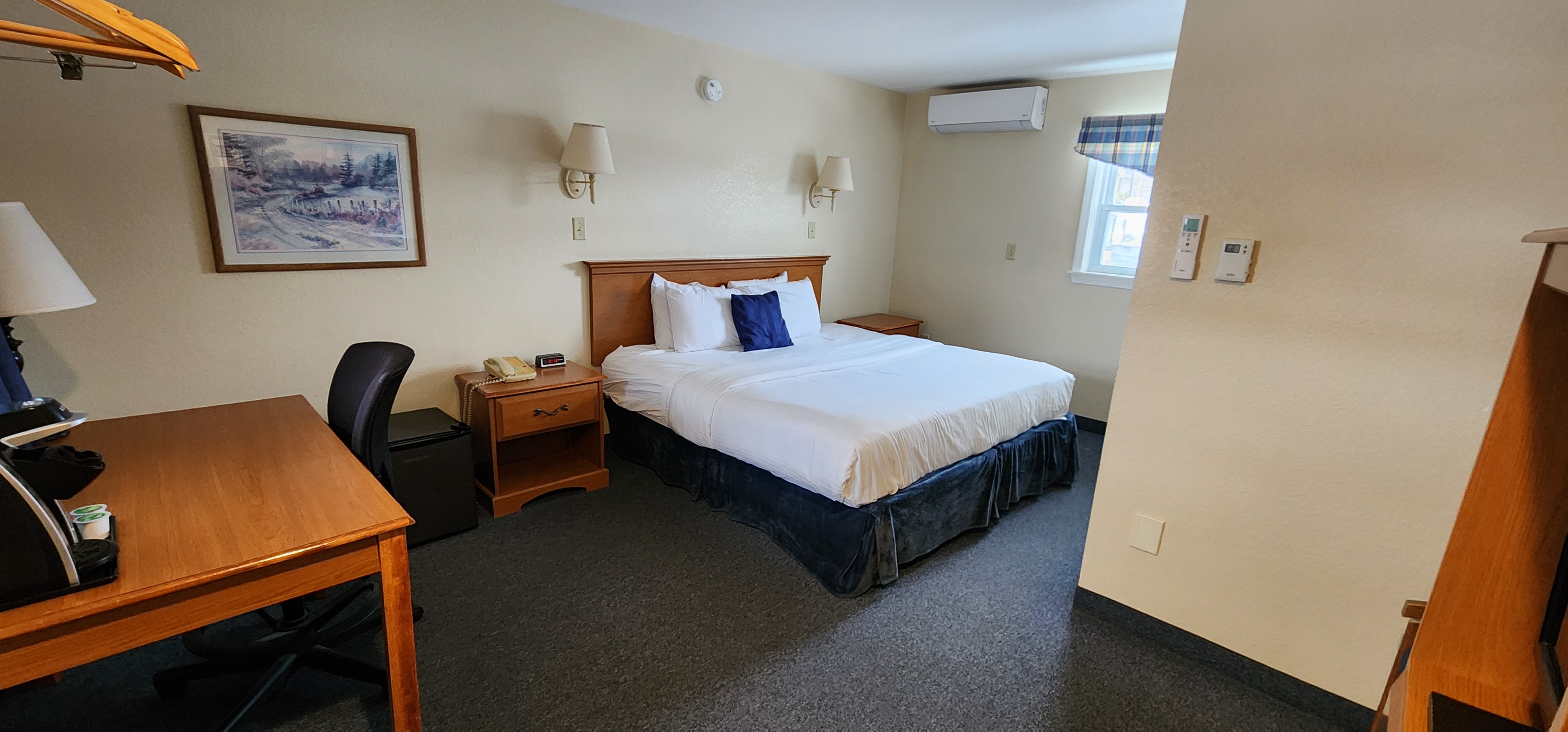 A hotel room with a bed, desk, chair, and window