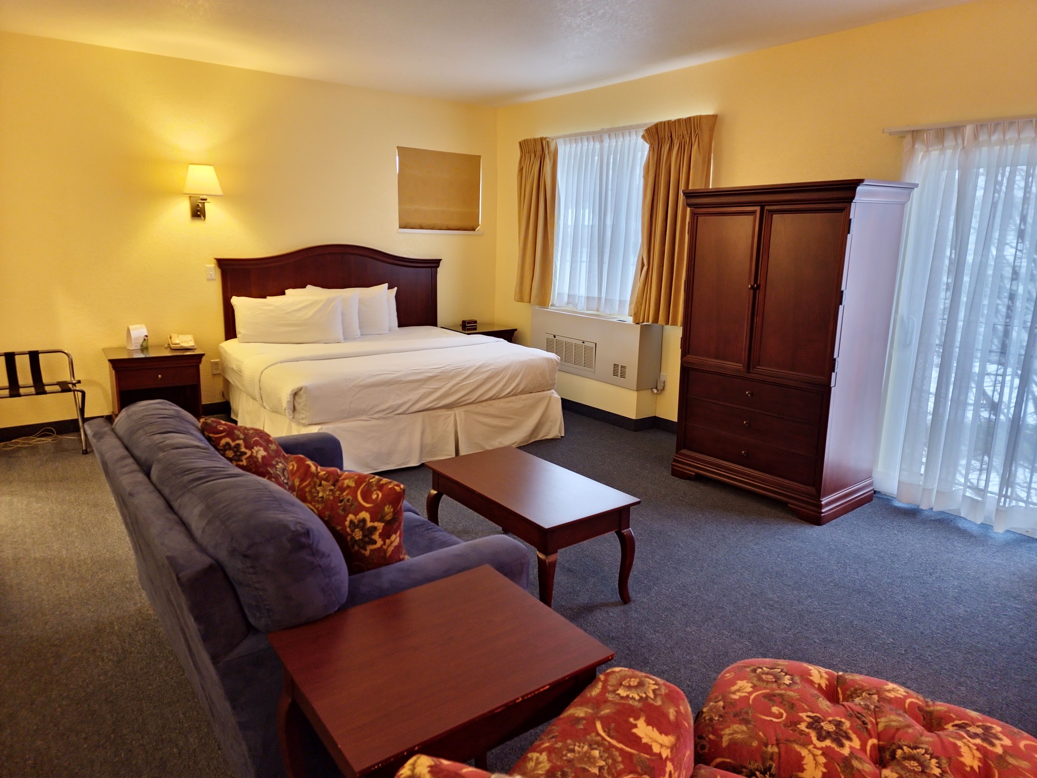 A wide view of a hotel room with a bed, sofa, coffee table, wardrobe, and window.